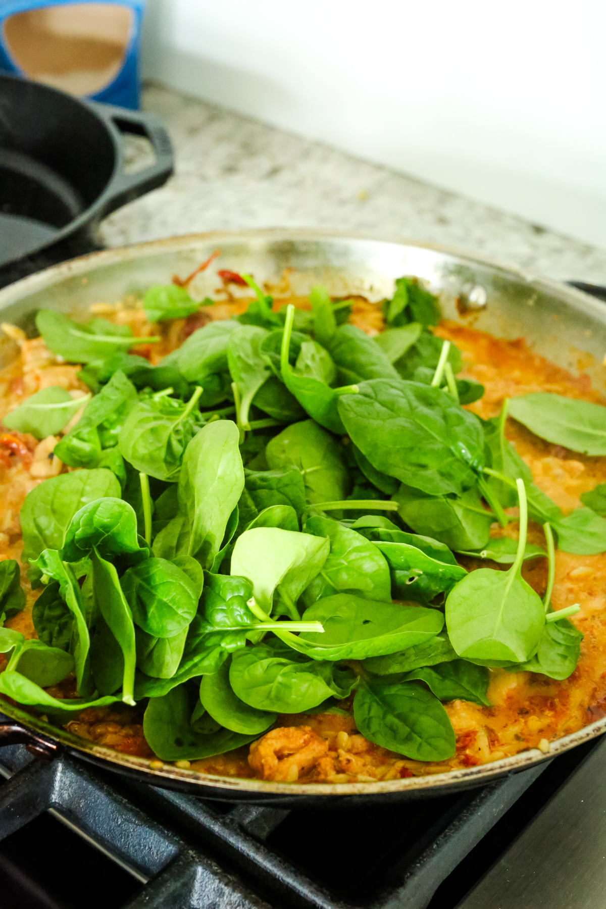 spinach on top of an orange liquid in a large skillet