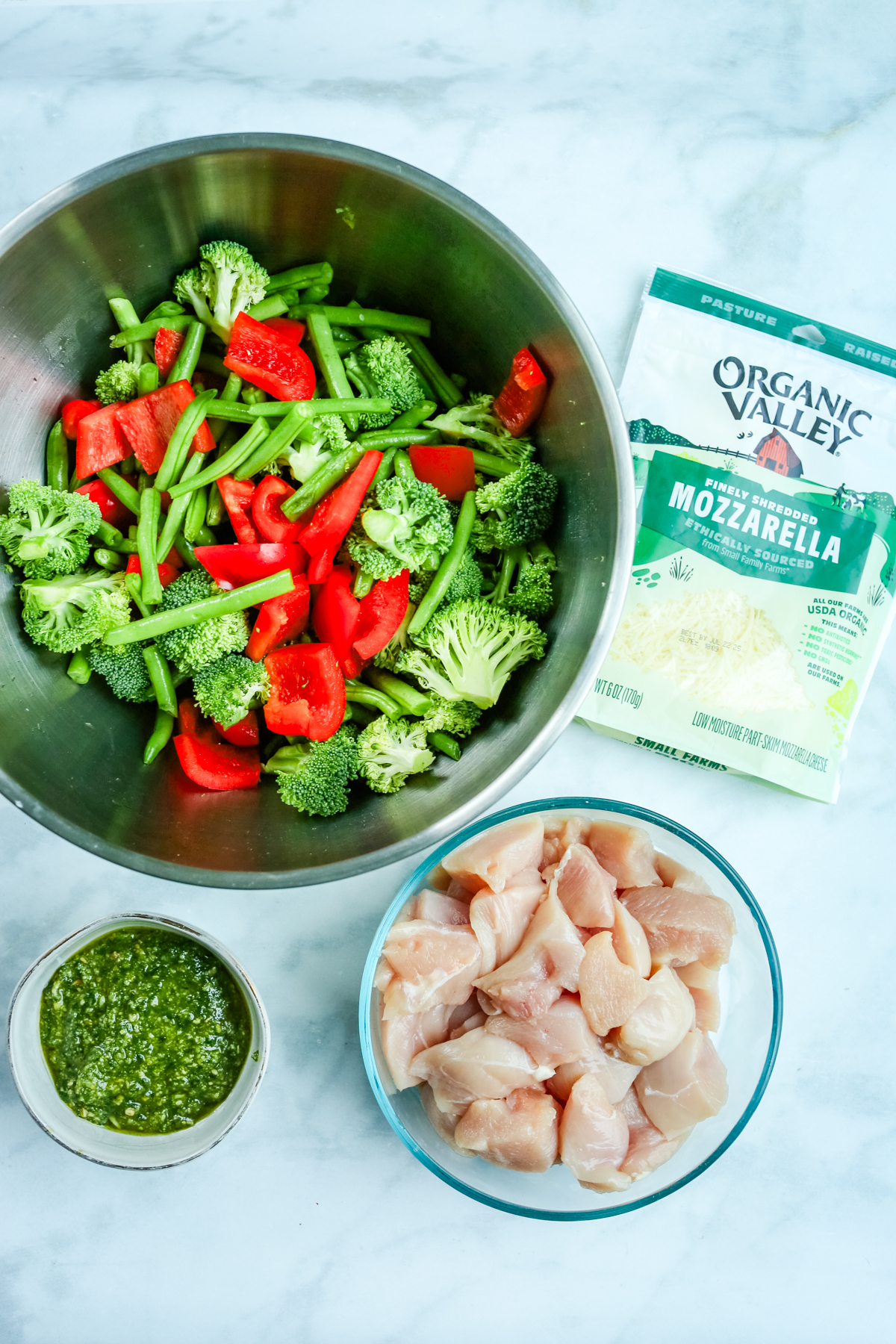 overhead shot of recipe ingredients: chicken, pesto, vegetables, and cheese