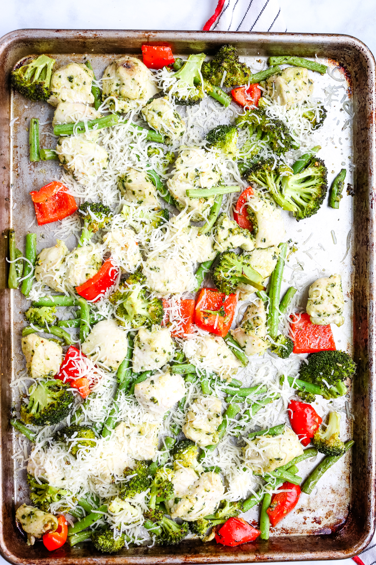 adding mozzarella cheese to the sheet pan of chicken and vegetables