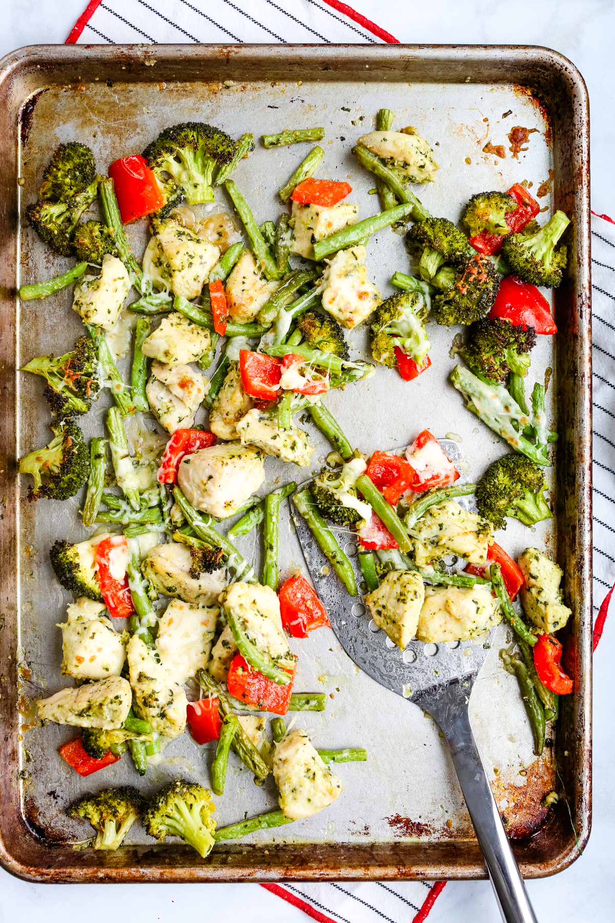sheet pan pesto chicken and vegetables after cooking in the oven with a spatula taking a serving