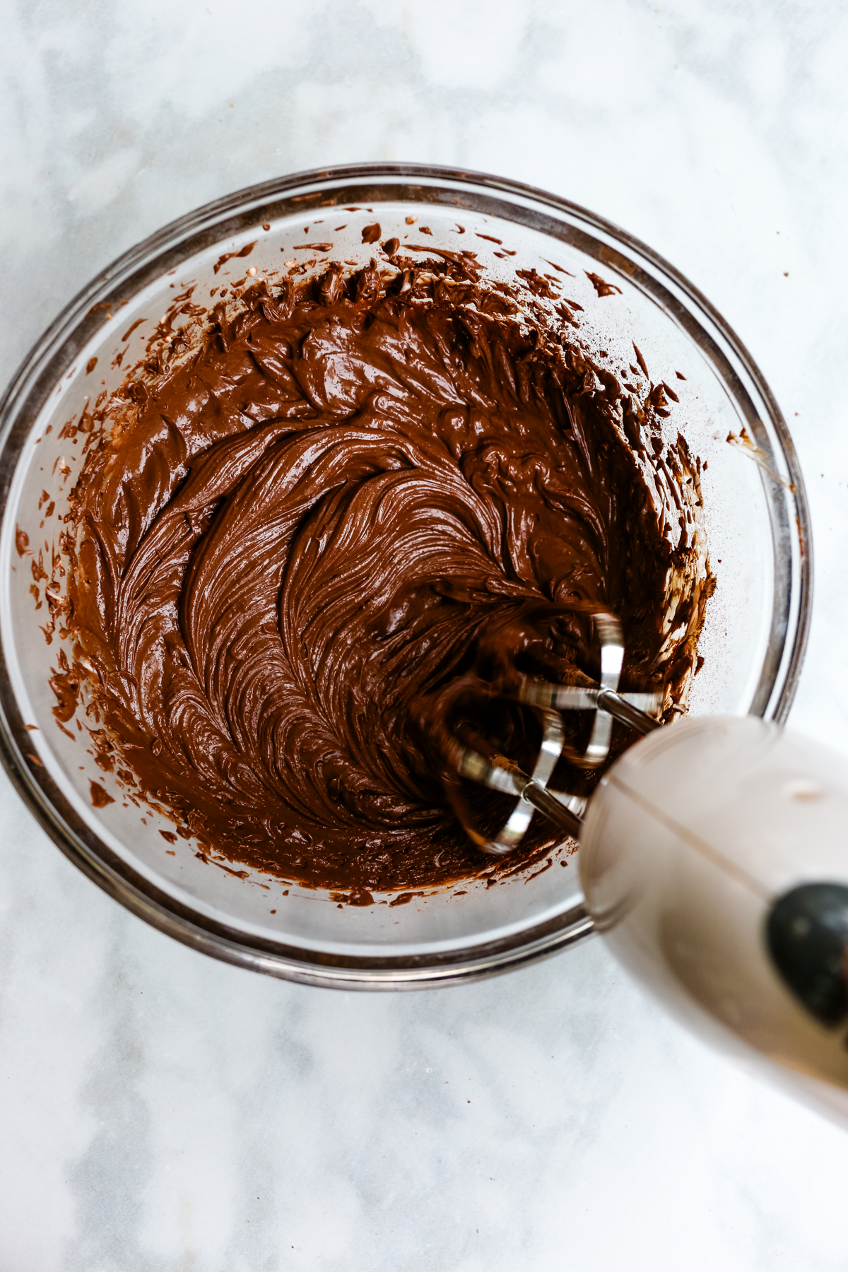 ingredients being blended with a hand mixer in a glass bowl