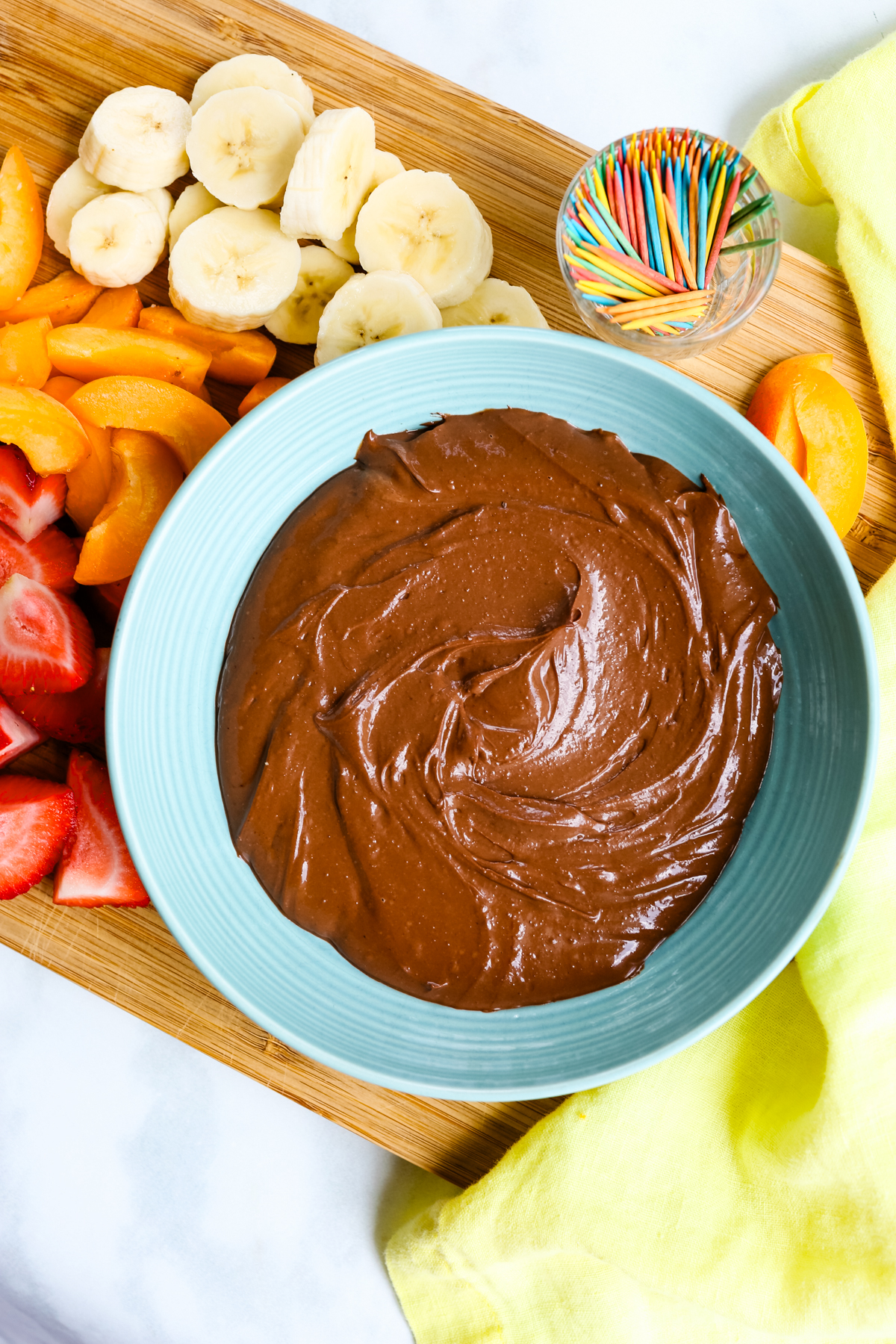 Chocolate Greek yogurt dip in a blue bowl on a wooden cutting board with fresh fruit