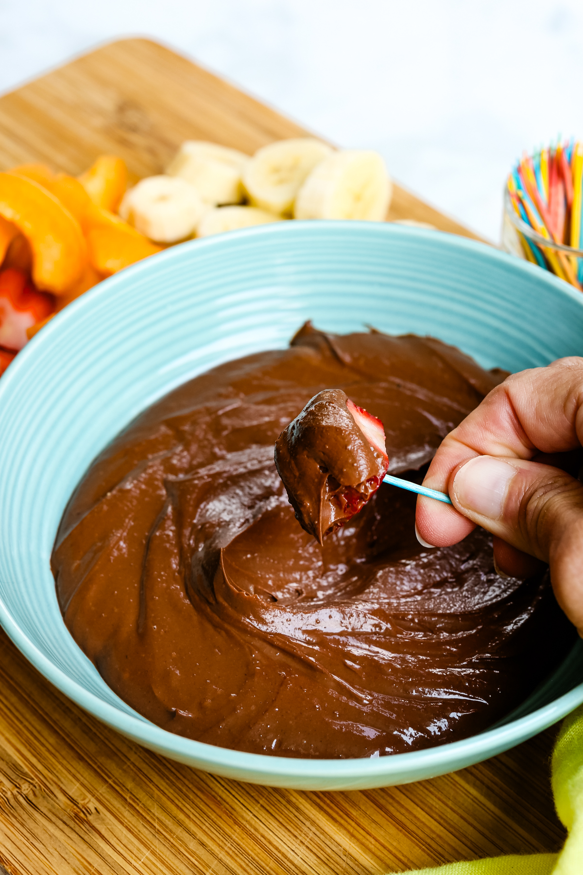 a strawberry on a toothpick being dipped into a bowl of Chocolate Greek Yogurt Dip