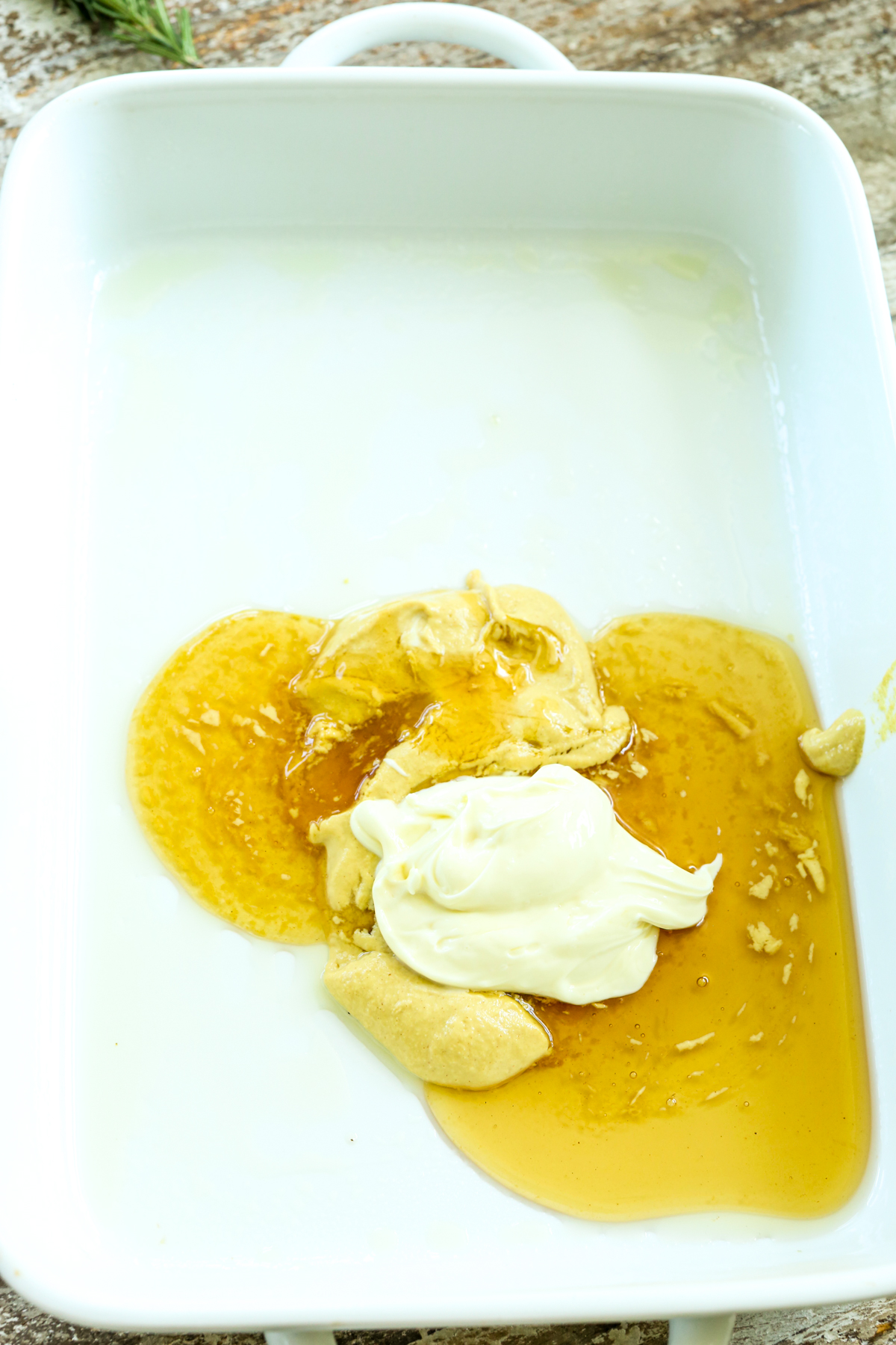 a white baking dish with mustard, honey, and mayo inside it but not mixed together