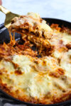 a skillet with lasagna recipe and a spatula taking out a serving