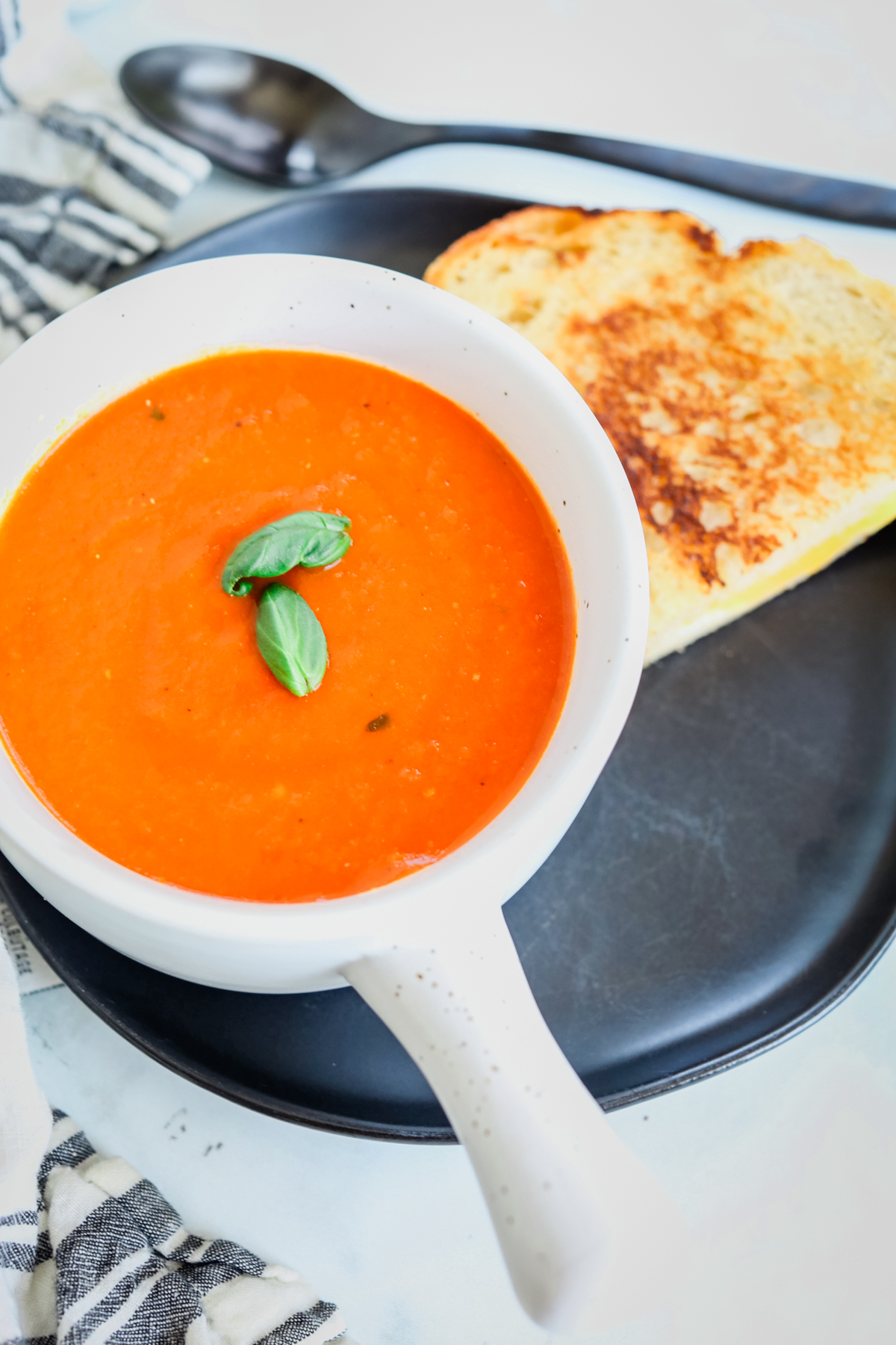 roasted tomato soup in a bowl with half of a grilled cheese sandwich on a plate