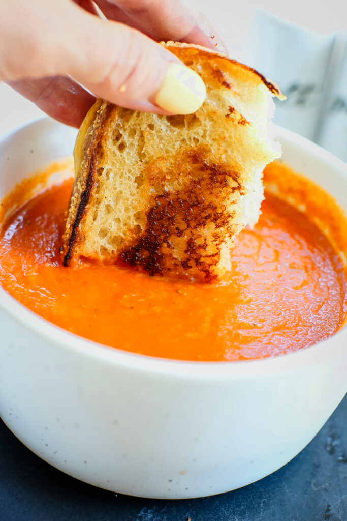 dipping a grilled cheese sandwich into a bowl of roasted tomato soup