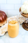 a pumpkin protein shake in a mason jar with a glass straw