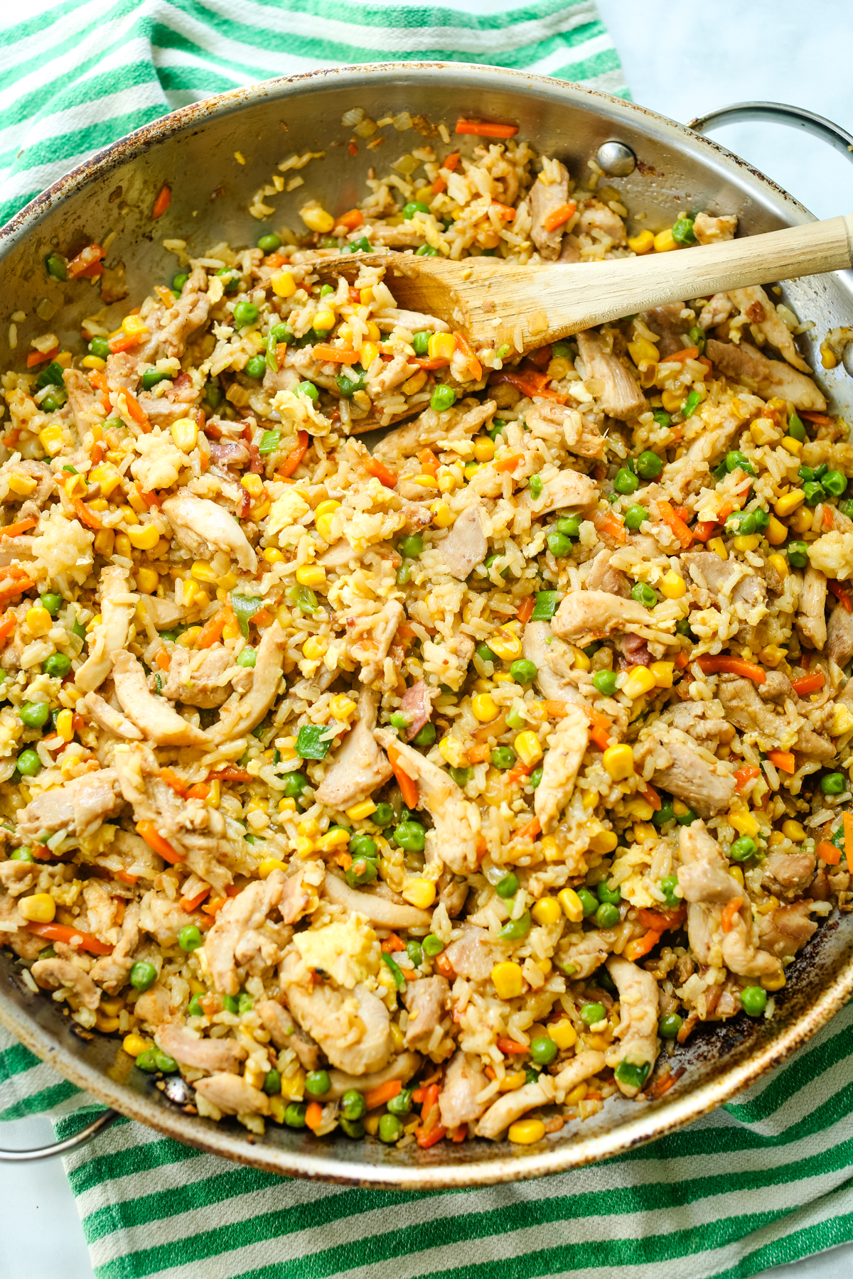 a large skillet of chicken fried rice with a wooden spoon
