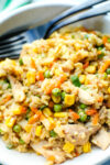 close up shot of chicken fried rice in a bowl with a fork and spoon at the edge of the bowl