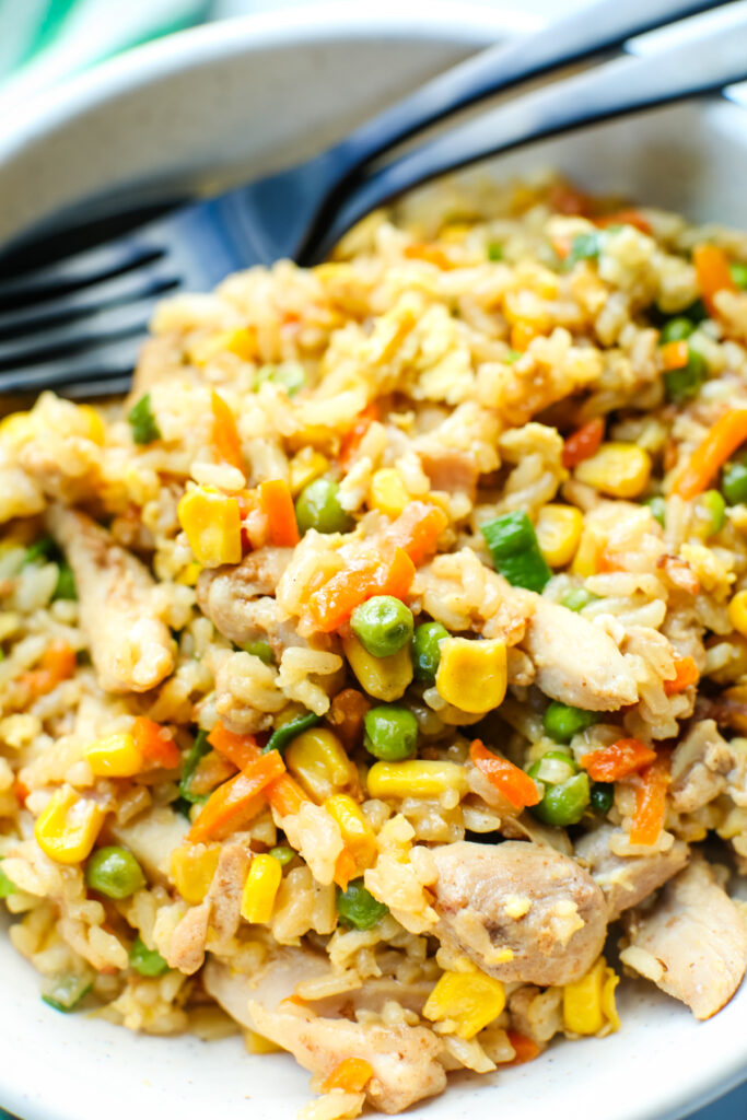 close up shot of chicken fried rice in a bowl with a fork and spoon at the edge of the bowl