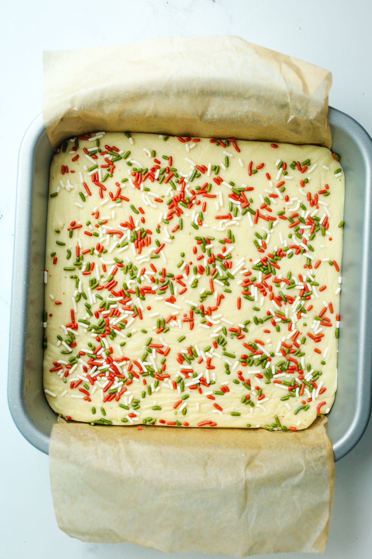 white chocolate fudge with red and green sprinkles in a pan with parchment paper