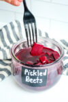 a jar of pickled beets with a black fork taking one out