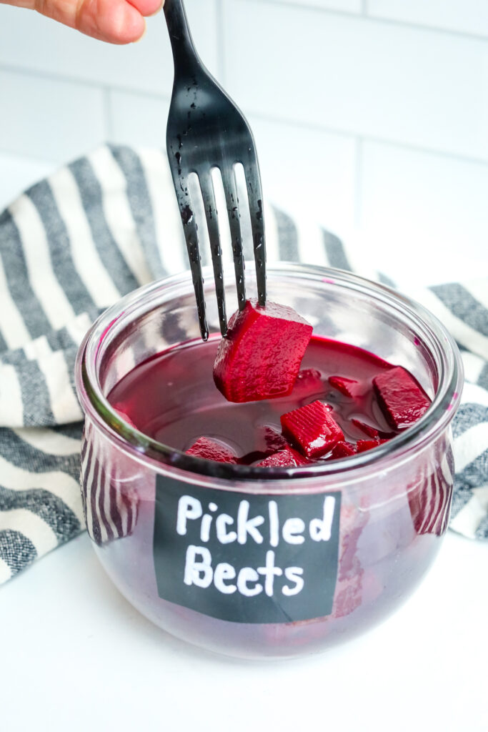 a jar of pickled beets with a black fork taking one out