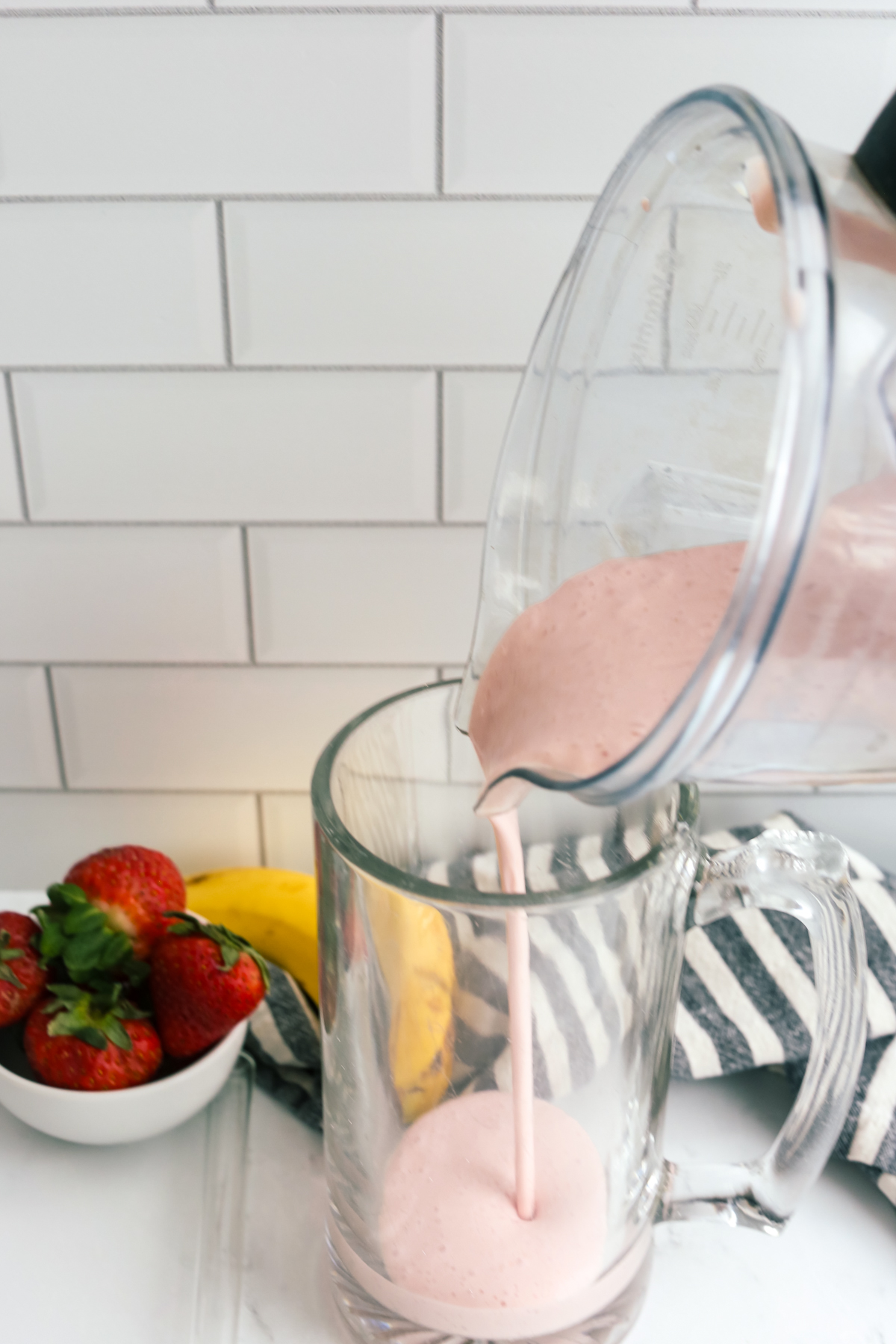 pouring a strawberry banana protein smoothie into a large glass mug