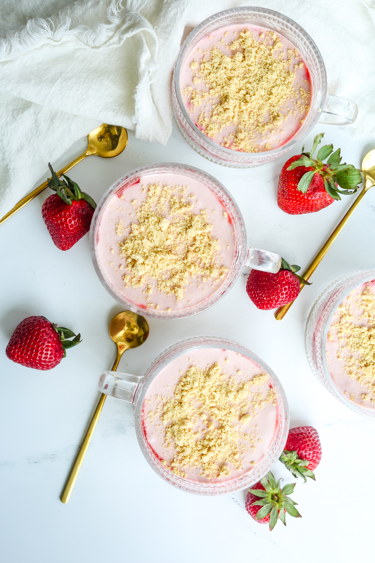 overhead shot of strawberry cheesecake parfaits in fancy glass cups with gold spoons