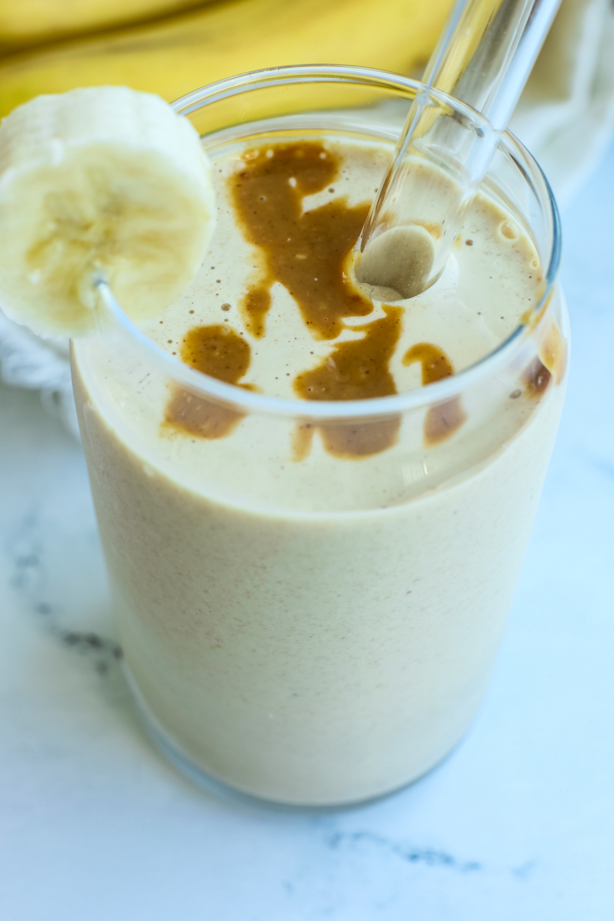 a close up photo of the banana peanut butter smoothie with a banana slice in the glass 