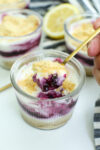 a photo of the no bake lemon blueberry cheesecake being scooped out of a small glass jar with a small gold spoon