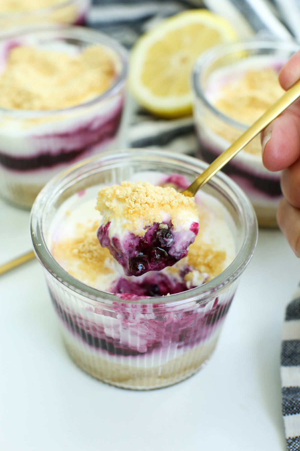 a photo of the no bake lemon blueberry cheesecake being scooped out of a small glass jar with a small gold spoon
