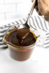 a Pyrex container with homemade enchilada sauce and a spoon dipping in