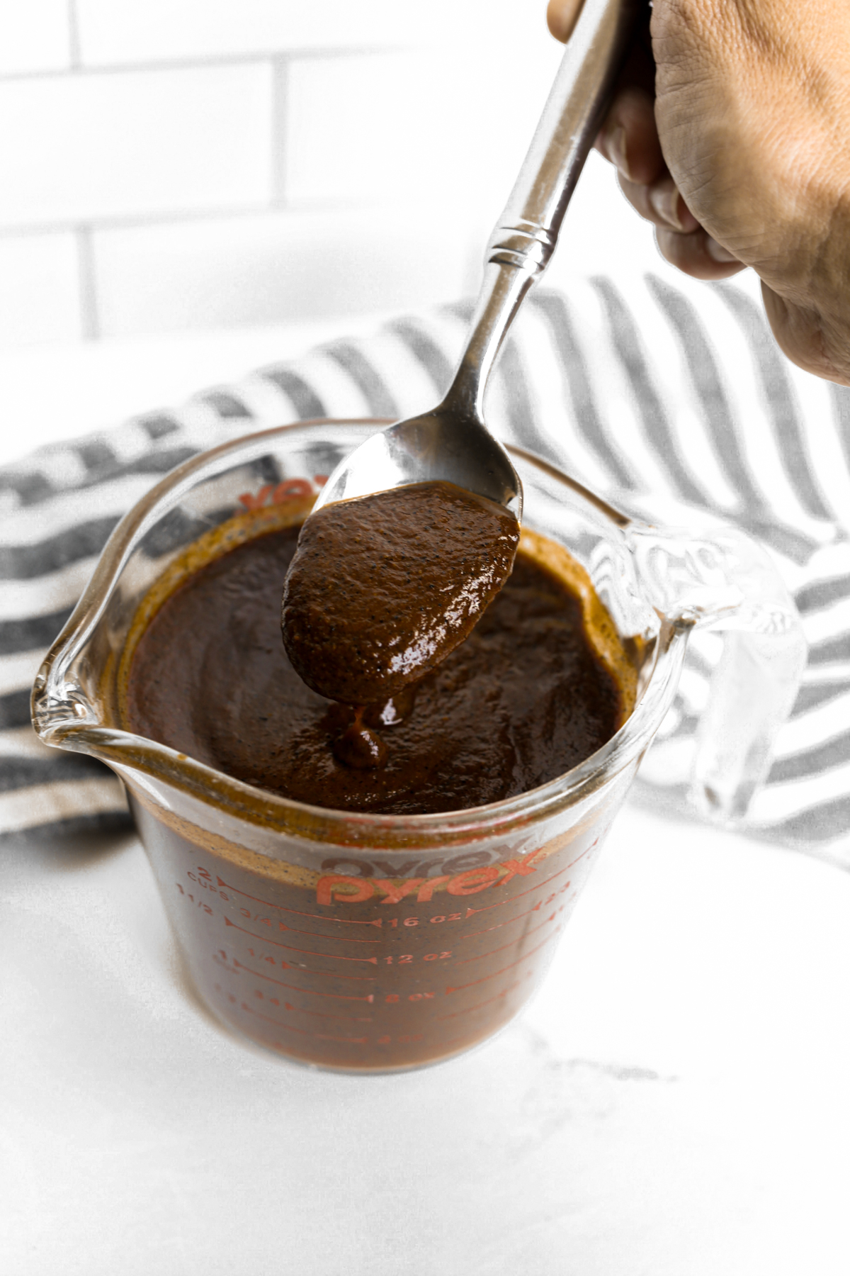 a Pyrex container with homemade enchilada sauce and a spoon dipping in